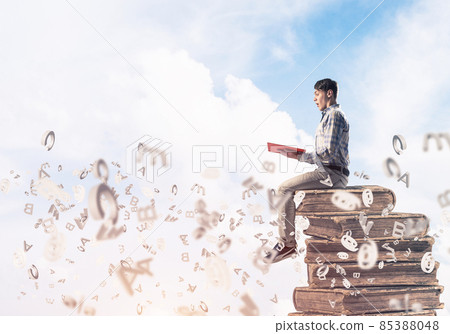 Man student on stack reading book and symbols flying around 85388048