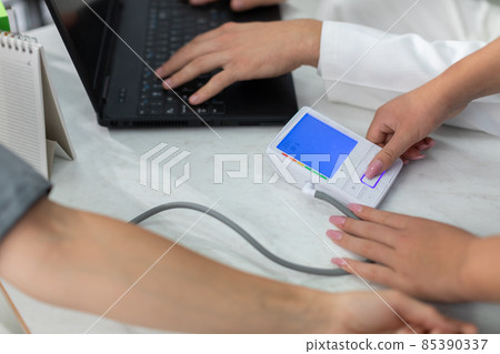 The nurse turns on the electronic blood pressure monitor to check blood pressure. 85390337