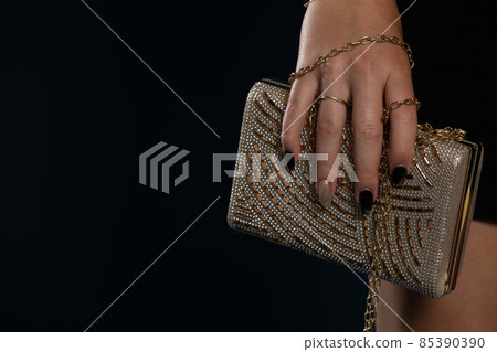 Ladies gold handbag in delicate ladies hand on navy blue background. 85390390