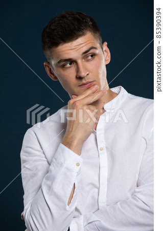 Portrait of a young handsome man wearing a long sleeved white shirt. He is looking to the side. 85390394