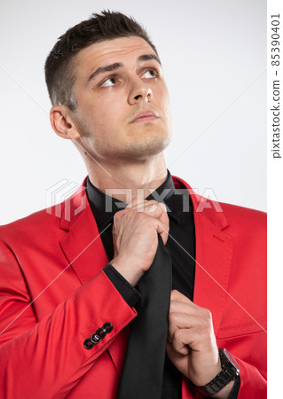 A young elegant man in a red blazer and black shirt, tweaks his tie. 85390401
