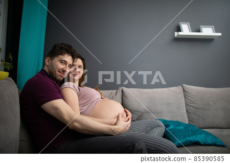 A married couple huddled sitting on a sofa looking straight into the lens. Pregnant woman. A married couple huddled sitting on a sofa looking straight into the lens. Pregnant woman. 85390585