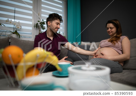 A married couple expecting a baby sits in their home. The pregnant woman. A married couple expecting a baby sits in their home. The pregnant woman. 85390593