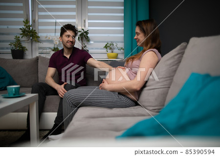 A married couple expecting a baby sits in their home. The pregnant woman. A married couple expecting a baby sits in their home. The pregnant woman. 85390594