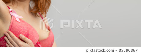 A young woman performs a breast self-examination by gently applying pressure with her hand. Pink ribbon - Symbol of the fight against breast cancer. Panorama 85390867