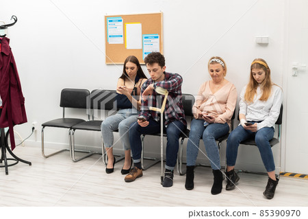 Patients sit in a clinic waiting for their turn to go to the doctor's office. They look at their cell phone while waiting. Patients sit in a clinic waiting for their turn to go to the doctor's office. They look at their cell phone while waiting. 85390970