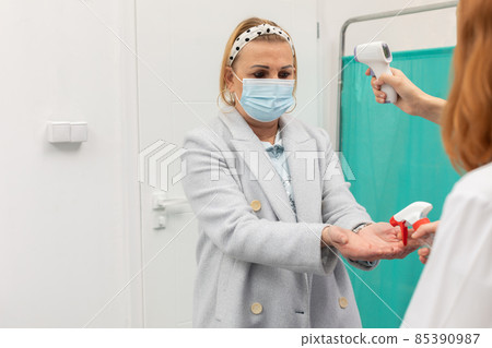 At the entrance to the clinic, the medical staff takes the temperature and disinfects the hands of all entering patients At the entrance to the clinic, the medical staff takes the temperature and disinfects the hands of all entering patients 85390987