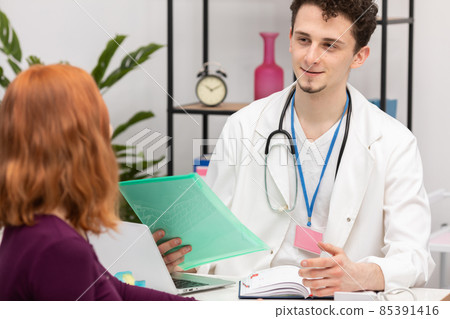 A doctor talks to a redheaded patient with a smile on his face. An adult woman in a doctor's office 85391416