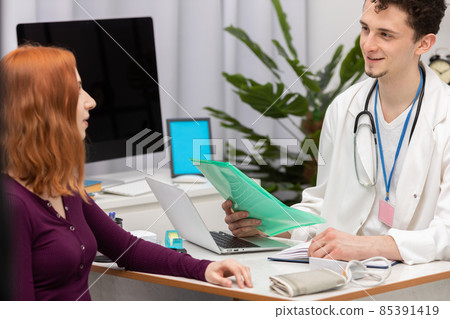 A doctor talks to a redheaded patient with a smile on his face. An adult woman in a doctor's office A doctor talks to a redheaded patient with a smile on his face. An adult woman in a doctor's office 85391419