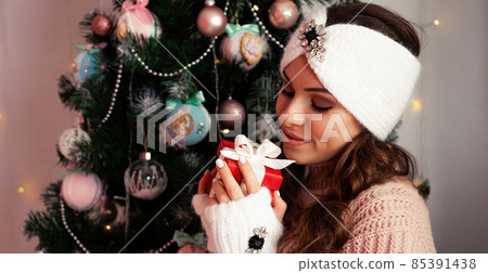 Happy woman holding a gift box on the background of a Christmas tree. Portrait of a happy smiling Happy woman holding a gift box on the background of a Christmas tree. Portrait of a happy smiling 85391438