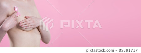 Undressed woman holds pink ribbon over breast pressing index finger against body. Panoramic frame. Undressed woman holds pink ribbon over breast pressing index finger against body. Panoramic frame. 85391717