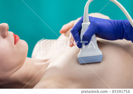 A lady doctor using ultrasound is examining a young patient's breasts. Doctor's office. Close-up view. 85391758