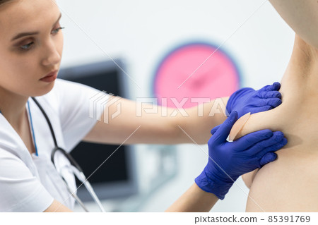 The doctor conducts a breast exam on a young patient, gently applying pressure with her hands. Close-up view. The doctor conducts a breast exam on a young patient, gently applying pressure with her hands. Close-up view. 85391769