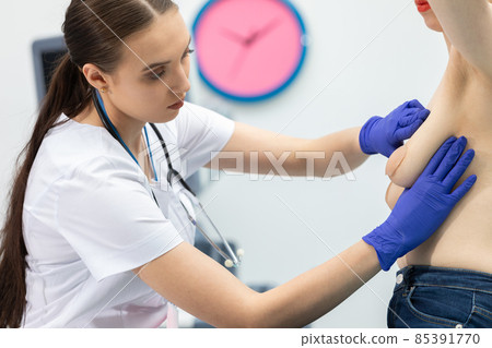 A doctor conducts a breast exam on a young patient, gently applying pressure with her hands. Doctor's office. A doctor conducts a breast exam on a young patient, gently applying pressure with her hands. Doctor's office. 85391770