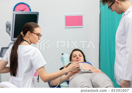 A nurse performs an ultrasound on a pregnant patient under the guidance of the attending doctor. 85391807