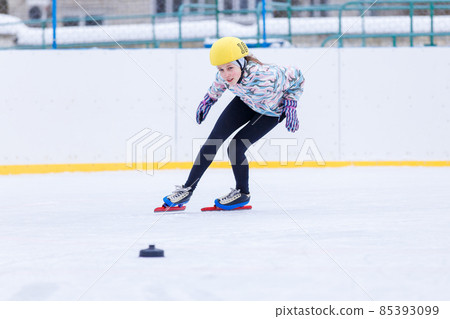 Slim teenage girl skating on the ice track on short treck training 85393099