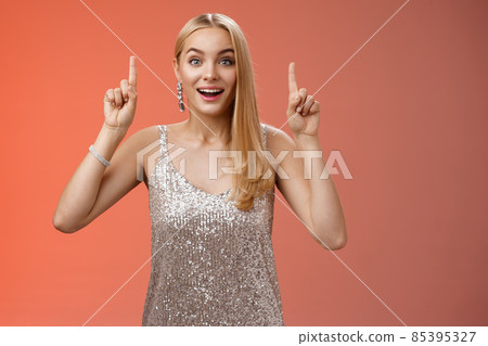 Charming amazed blond european woman in fabulous silver glittering dress raise hands point up amused enjoying watching shooting stars, fireworks gaze camera excited happy surprised, red background Charming amazed blond european woman in fabulous silver glittering dress raise hands point up amused enjoying watching shooting stars, fireworks gaze camera excited happy surprised, red background 85395327