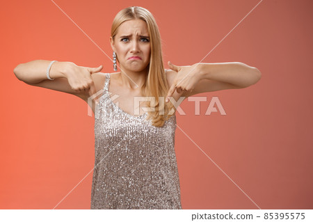 Whining complaining upset depressed blond woman in silver dress crying boyfriend broke-up prom night standing unhappy expressing sorrow regret disappointment pointing down red background 85395575