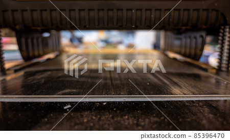 Selective focus looking into a wood planer bed raised above the board 85396470