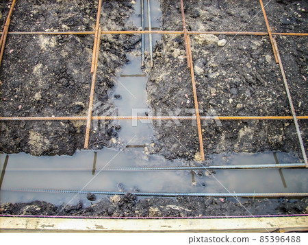 Construction site rebar suspended over a footing trench filled with rain water. Construction site rebar suspended over a footing trench filled with rain water. 85396488