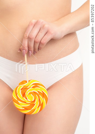 Hand of a woman wearing white panties holding lollipop on a stick covering the intimate area, the concept of intimate depilation, problems of intimate hygiene. Hand of a woman wearing white panties holding lollipop on a stick covering the intimate area, the concept of intimate depilation, problems of intimate hygiene. 85397202