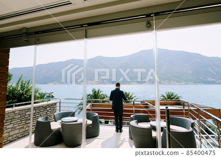 Man stands on the terrace of a luxury hotel and looks out to the sea. Back view Man stands on the terrace of a luxury hotel and looks out to the sea. Back view 85400475