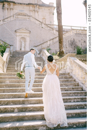 The bride and groom climbing the stairs of the Nativity of the Blessed Virgin Mary church in Prcanj and holding hands 85400545
