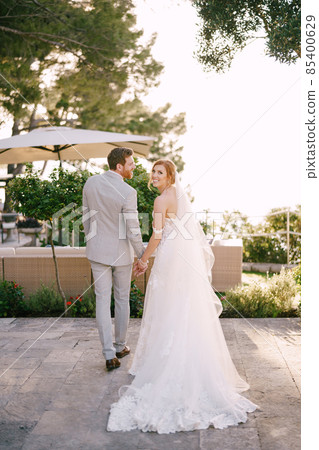 Bride and groom hold hands while standing near the armchairs under an umbrella from the sun 85400629