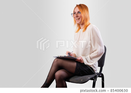 A girl, in a white blouse, with a folder in her hands, laughs cheerfully, on a gray background A girl, in a white blouse, with a folder in her hands, laughs cheerfully, on a gray background 85400630