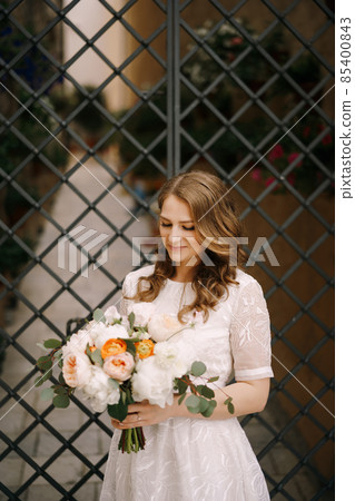 Bride in a white dress with a bouquet of flowers stands near the decorative gate Bride in a white dress with a bouquet of flowers stands near the decorative gate 85400843