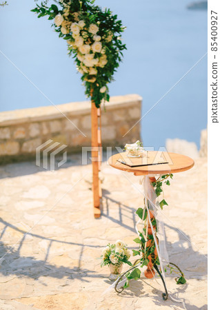 Small table stands in front of the wedding arch on an observation deck overlooking the sea Small table stands in front of the wedding arch on an observation deck overlooking the sea 85400927