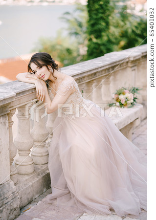Bride sits on a stone bench with her head resting on a stone balustrade Bride sits on a stone bench with her head resting on a stone balustrade 85401032