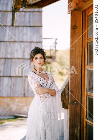 Woman in a white lace dress stands at the door of an old hut Woman in a white lace dress stands at the door of an old hut 85401033