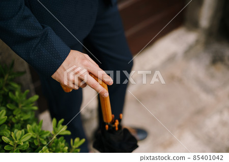 Man hand rests on the wooden cane of the umbrella. Close-up 85401042