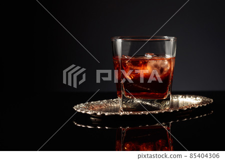Whiskey with ice on a black reflective background. Whiskey with ice on a black reflective background. 85404306