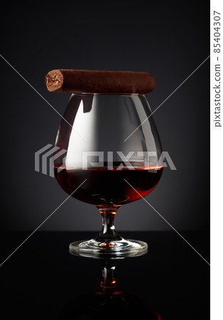 Snifter of brandy and cigar on a black background. Snifter of brandy and cigar on a black background. 85404307