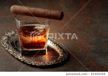 Whiskey with ice and cigar on a rusty background. Whiskey with ice and cigar on a rusty background. 85404308