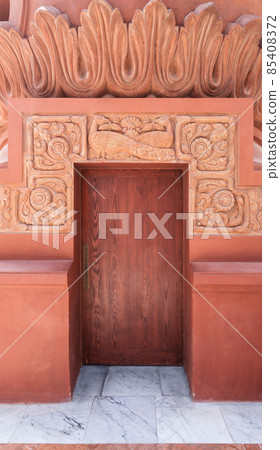 Recessed closed wooden door in ornamental stone wall outside of old building 85408372