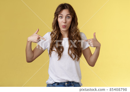 Wow just look. Impressed surprised cute wondered european girl pointing fingers center copy space white t-shirt folding lips amused astonished awesome promo great chance gaze you camera 85408798