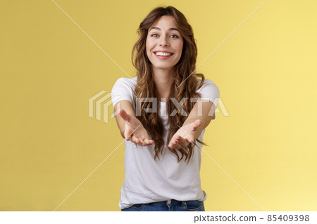 Let me hold it. Sincere tender touched charming curly-haired girl reaching you extend arms smiling lovely tempting grab precious thing receive gift stand yellow background grateful cheerful 85409398