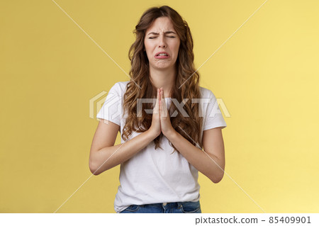 Please beg you. Sobbing timid insecure distressed cute whining girl crying upset close eyes grimacing hold hands pray pleading asking favour apologizing sincere hope for pity yellow background 85409901