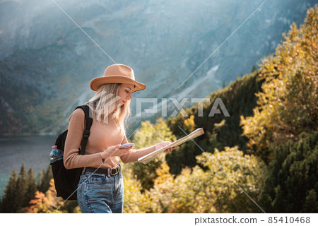 Wanderlust and travel concept. Stylish traveler girl in hat looking at map, exploring woods. Wanderlust and travel concept. Stylish traveler girl in hat looking at map, exploring woods. 85410468