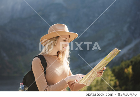 Wanderlust and travel concept. Stylish traveler girl in hat looking at map, exploring woods. 85410470