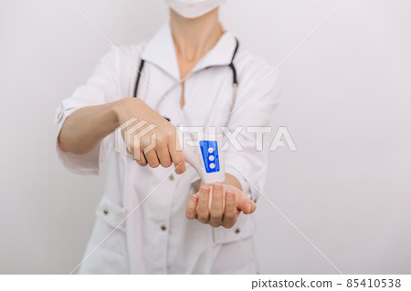 Temperature measurement gun in doctor hands. Close-up shot of doctor wearing protective surgical mask ready to use infrared isometric thermometer gun to check body temperature for virus symptoms. 85410538
