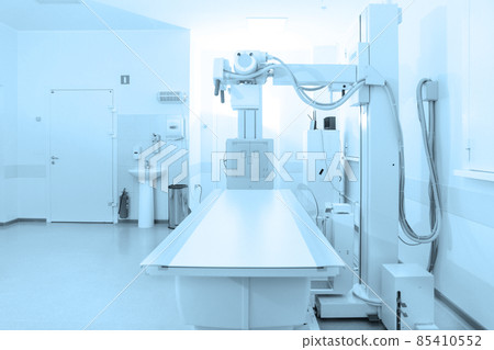 X-ray department in modern hospital. Radiology room with scan machine with empty bed. Technician adjusting an x-ray machine. Scanning chest, heart, lungs in modern clinic office. 85410552