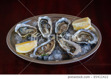 An exquisite and expensive dish of sea clams of oysters with ice and lemon on an iron plate on a wooden table. 85411422