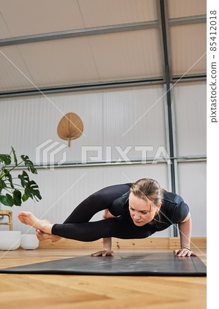 Athletic woman doing the advanced yoga posture Crow pose, kakasana. 85412018