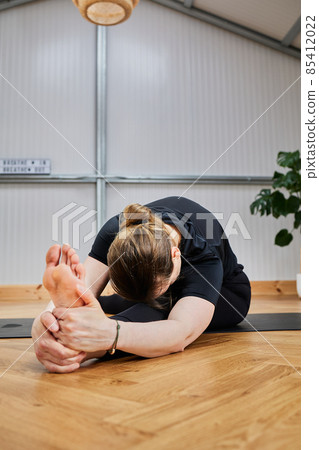 young woman with great flexibility touching her toes with her hands on a yoga mat.