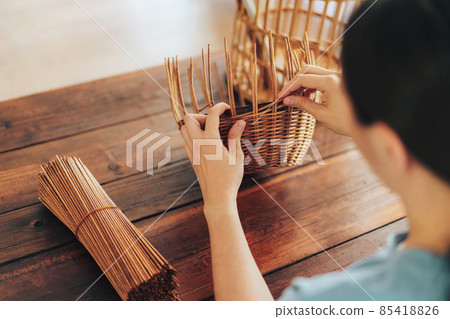 Woman weaves basket of paper tubes on wooden table Woman weaves basket of paper tubes on wooden table 85418826