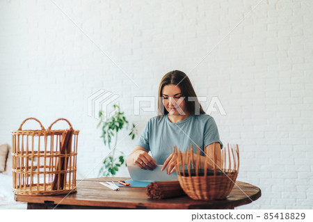 Woman sitting at table preparing basket weaving material Woman sitting at table preparing basket weaving material 85418829